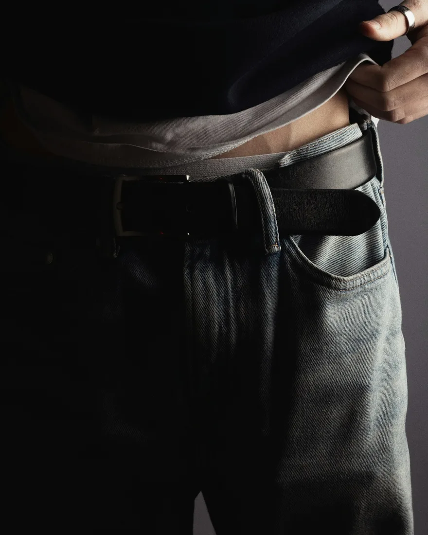 Détail d’un jean ample bleu gris porté avec une ceinture noire