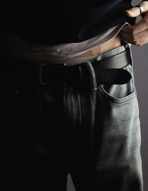 Détail d’un jean bleu gris porté avec une ceinture